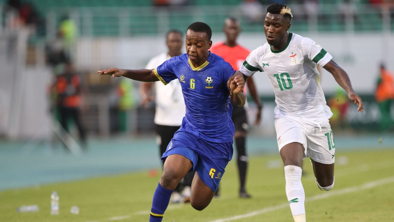  Mchezaji wa Tanzania (jezi ya bluu) akijaribu kumtoka beki wa Zambia (jezi ya machungwa) kwenye mechi ya kufuzu Kombe la Dunia 2026.